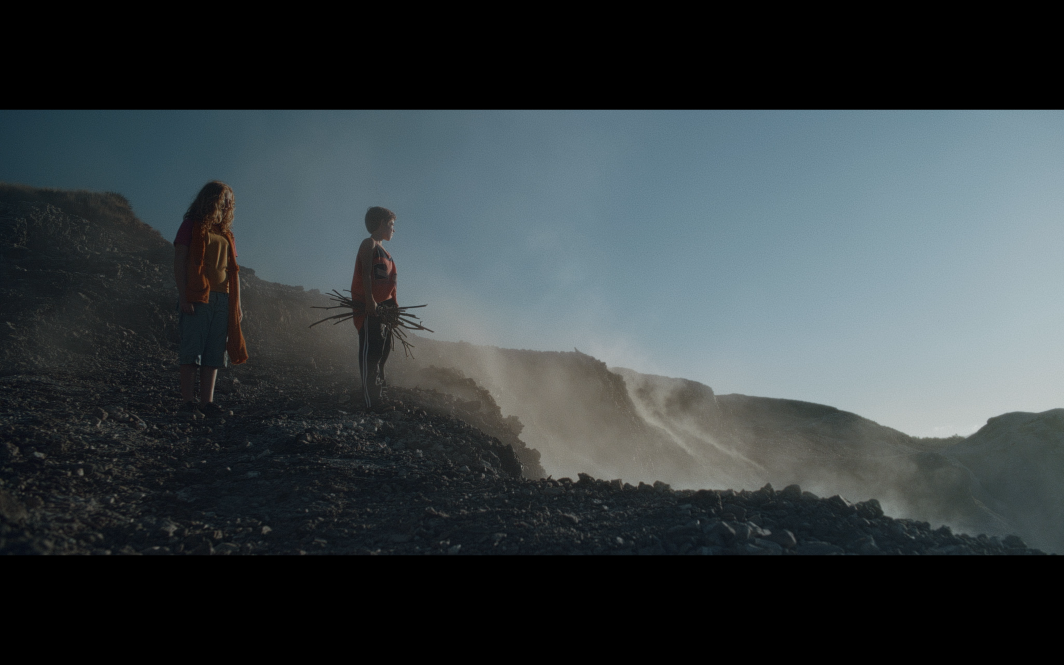 Two children standing on a rocky coast in mist