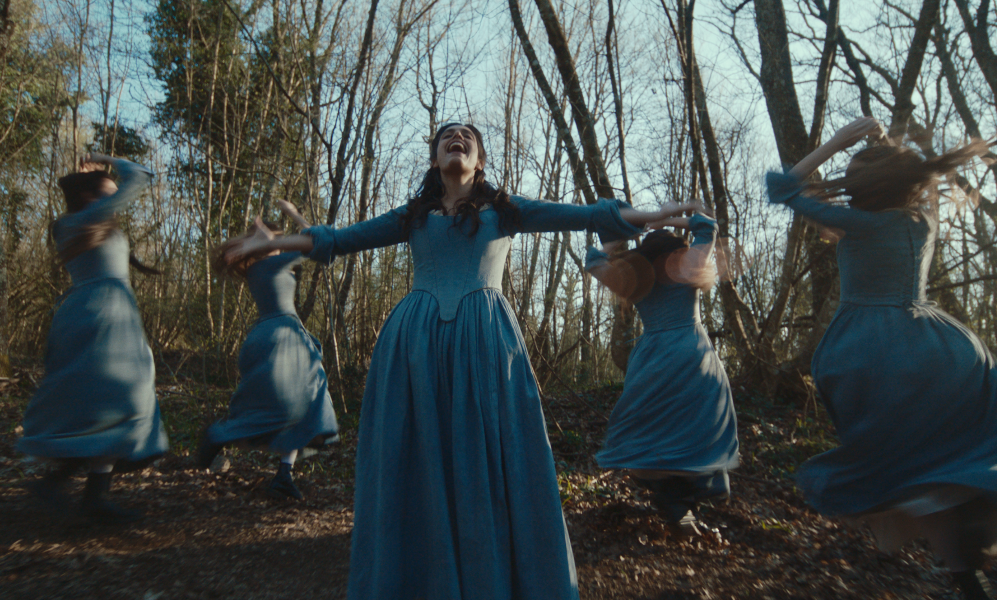 A group of women in blue dresses dancing among the trees