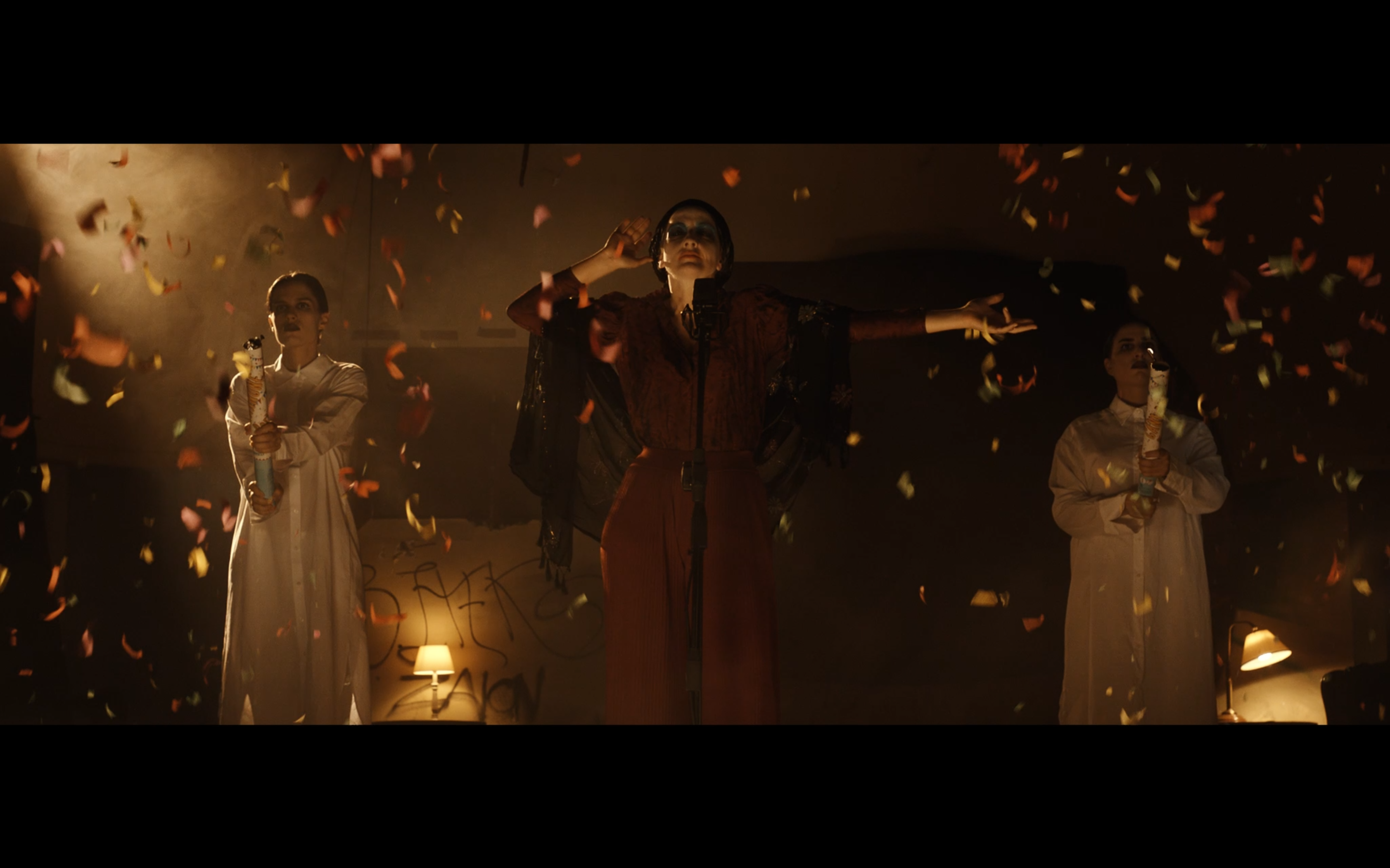 Three performers surrounded by confetti in a warmly lit room