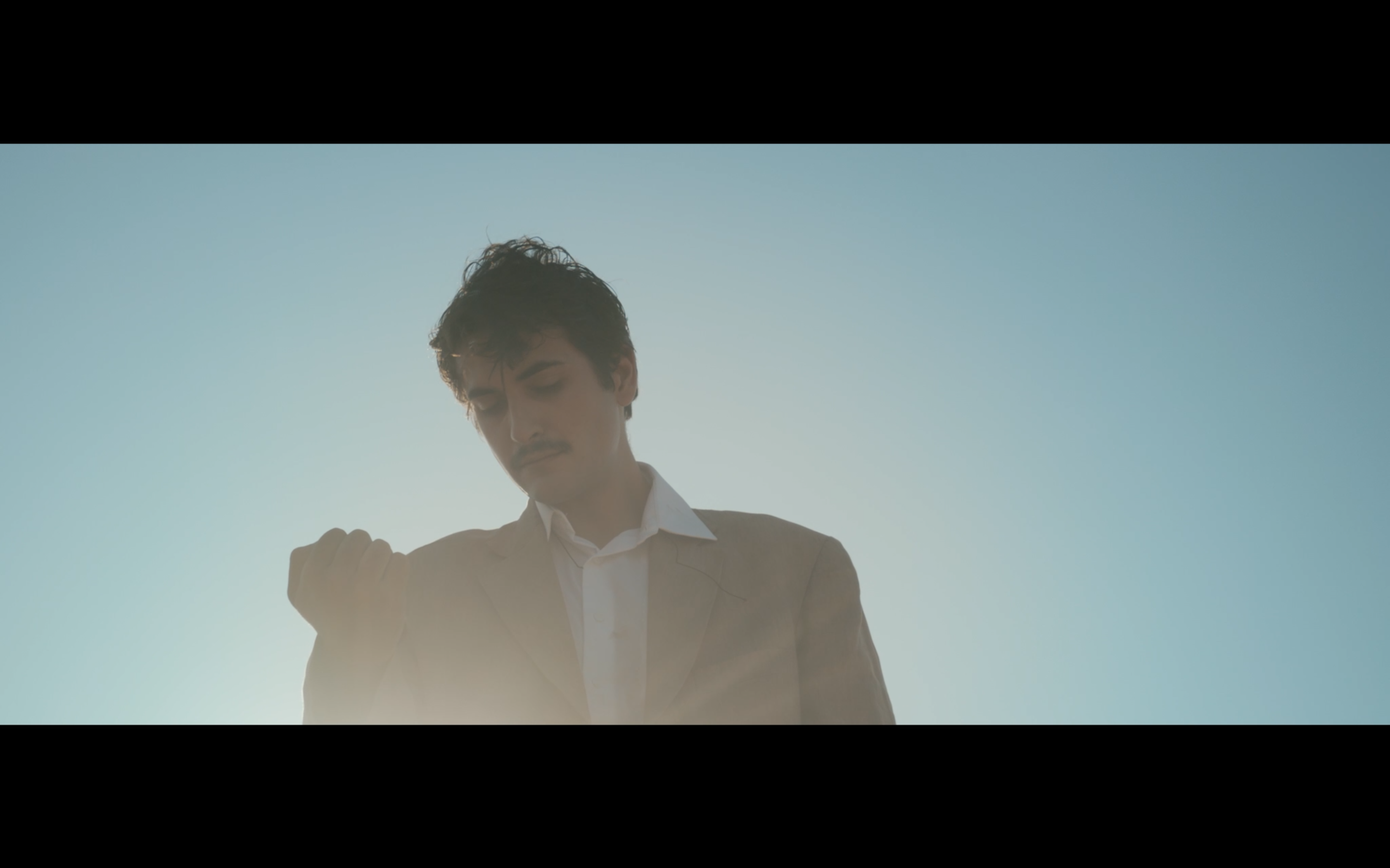 A man looking at his hand beneath a blue sky