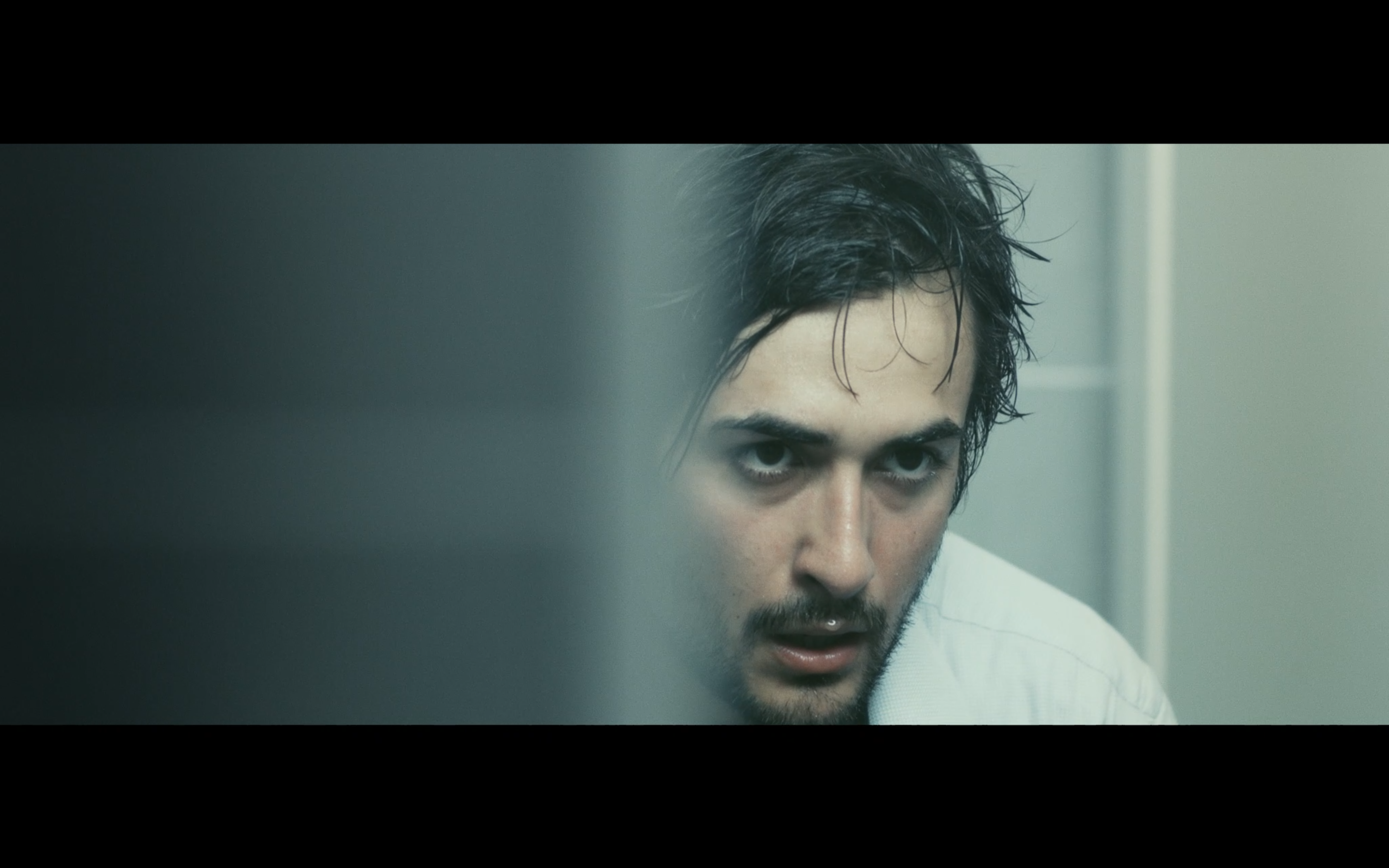 A close-up of a man in a cool-lit bathroom