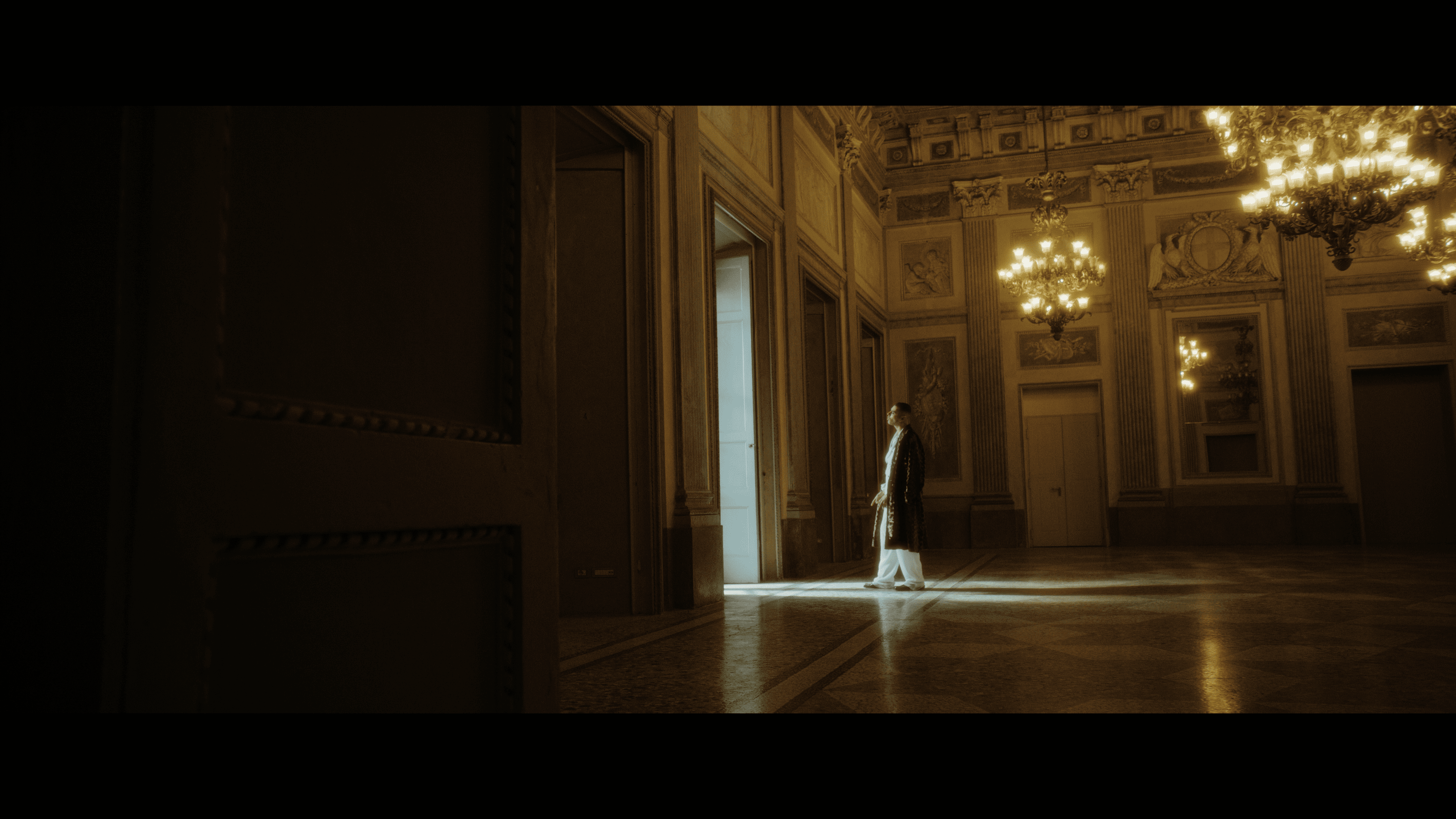 An artist crossing a large room beneath chandeliers