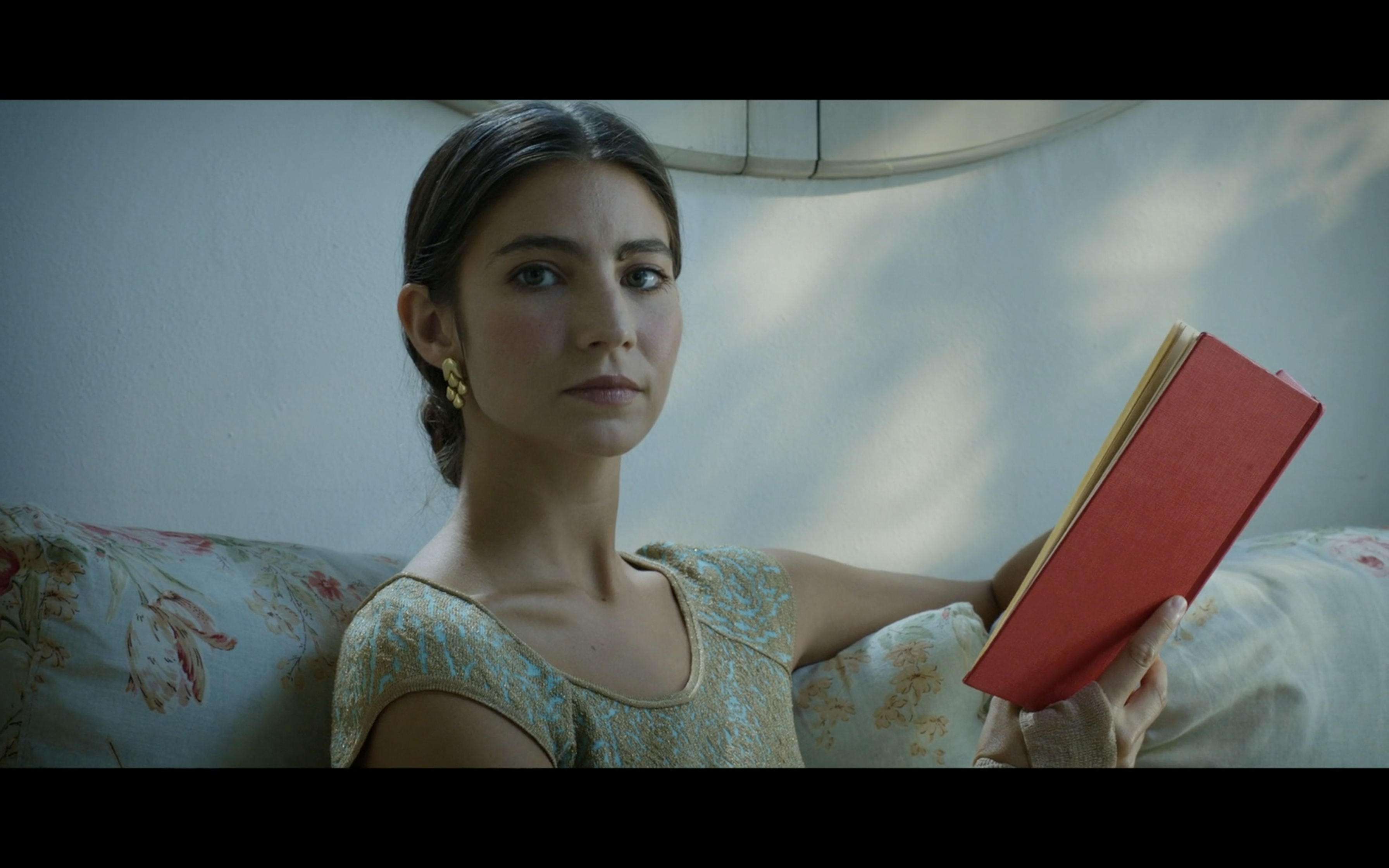 A woman holding a red book on a floral sofa