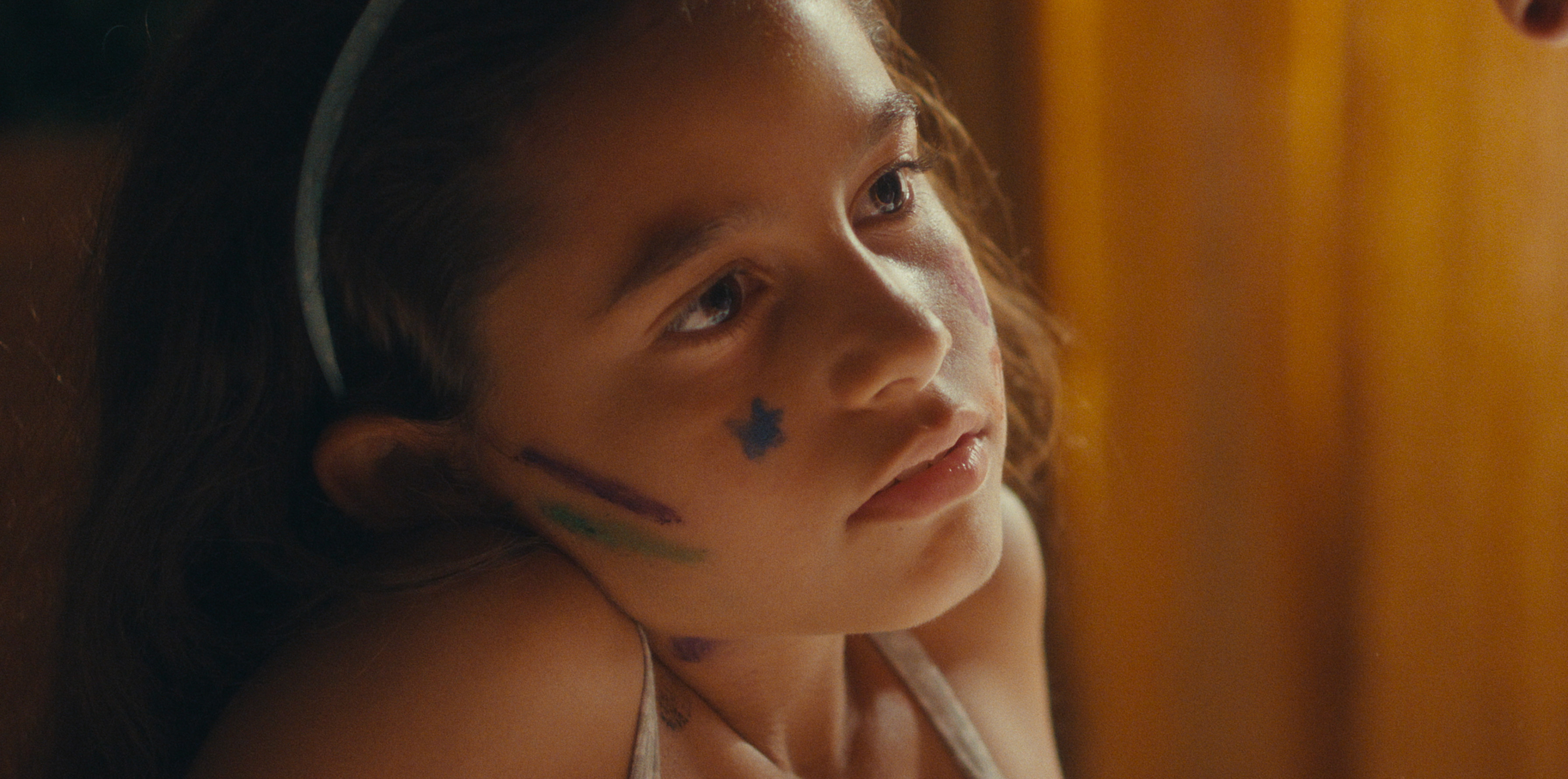 A child with drawings on her cheek looking up in warm light