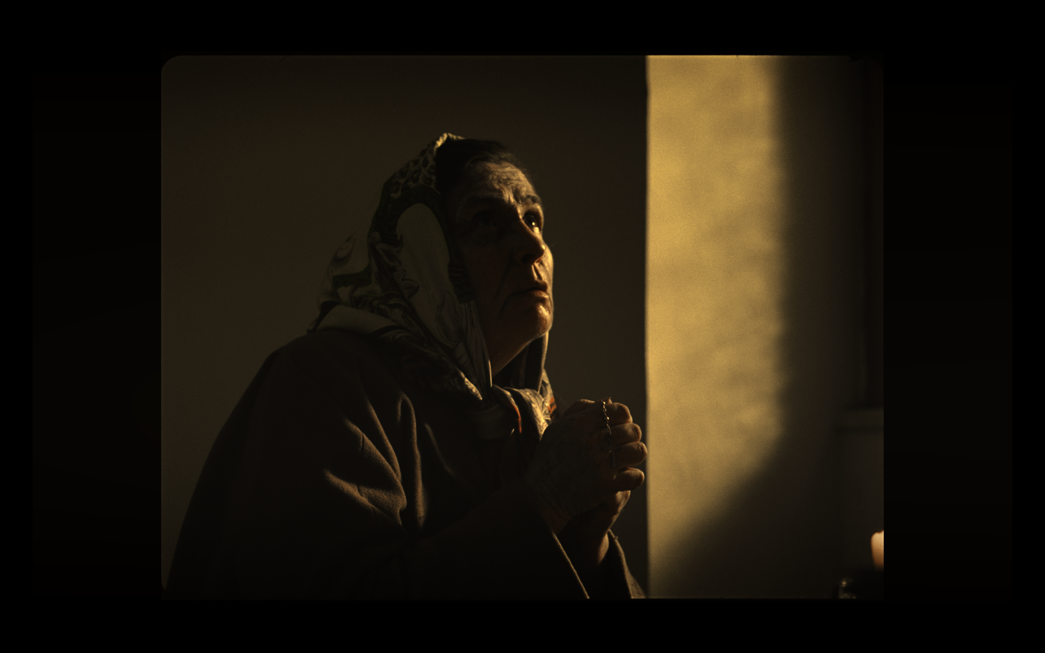 An older woman praying in warm light