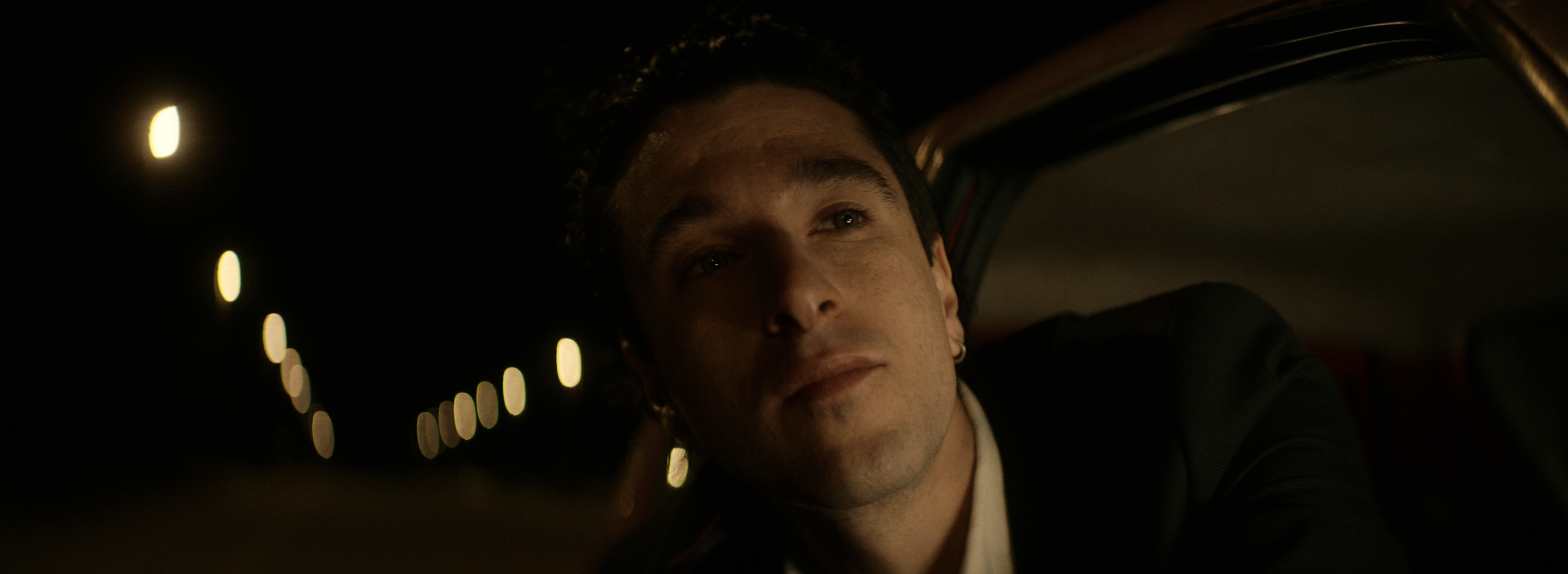 A close-up of a young man beside a car at night