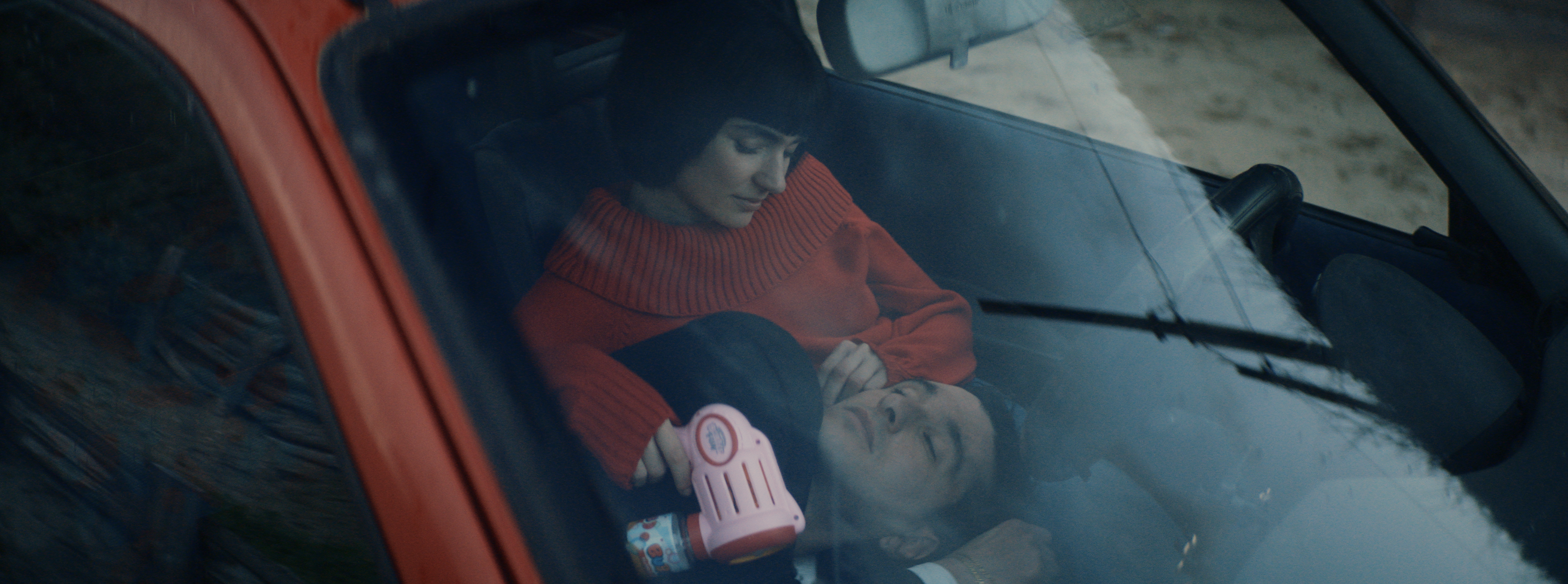 A couple resting inside a red car seen through the windshield