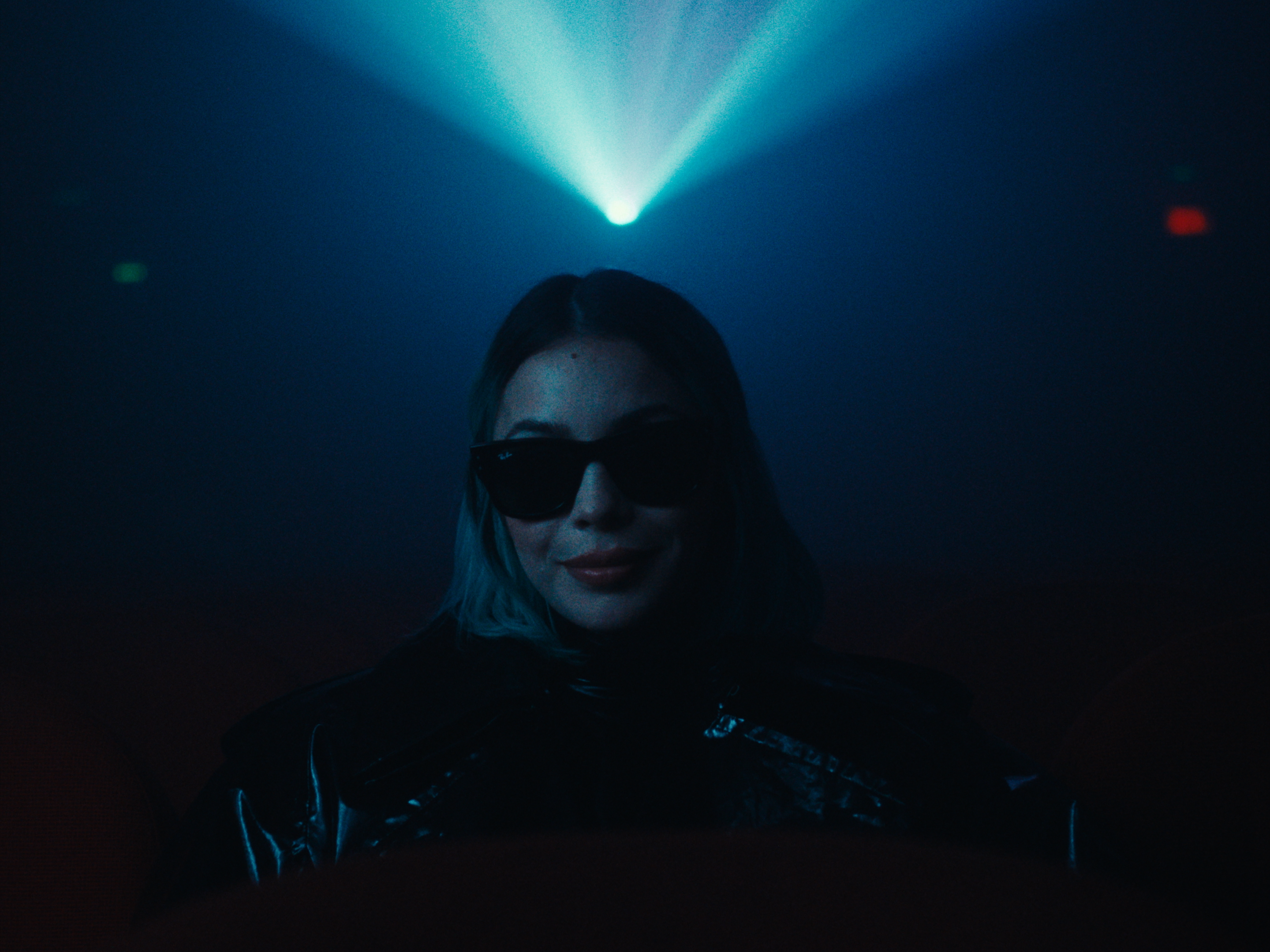 A woman wearing sunglasses beneath a beam of blue light