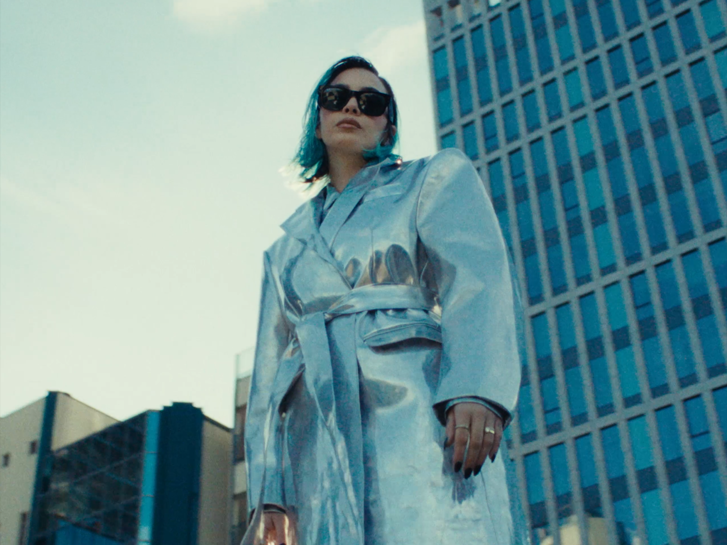 A woman wearing a silver coat beside a tall building