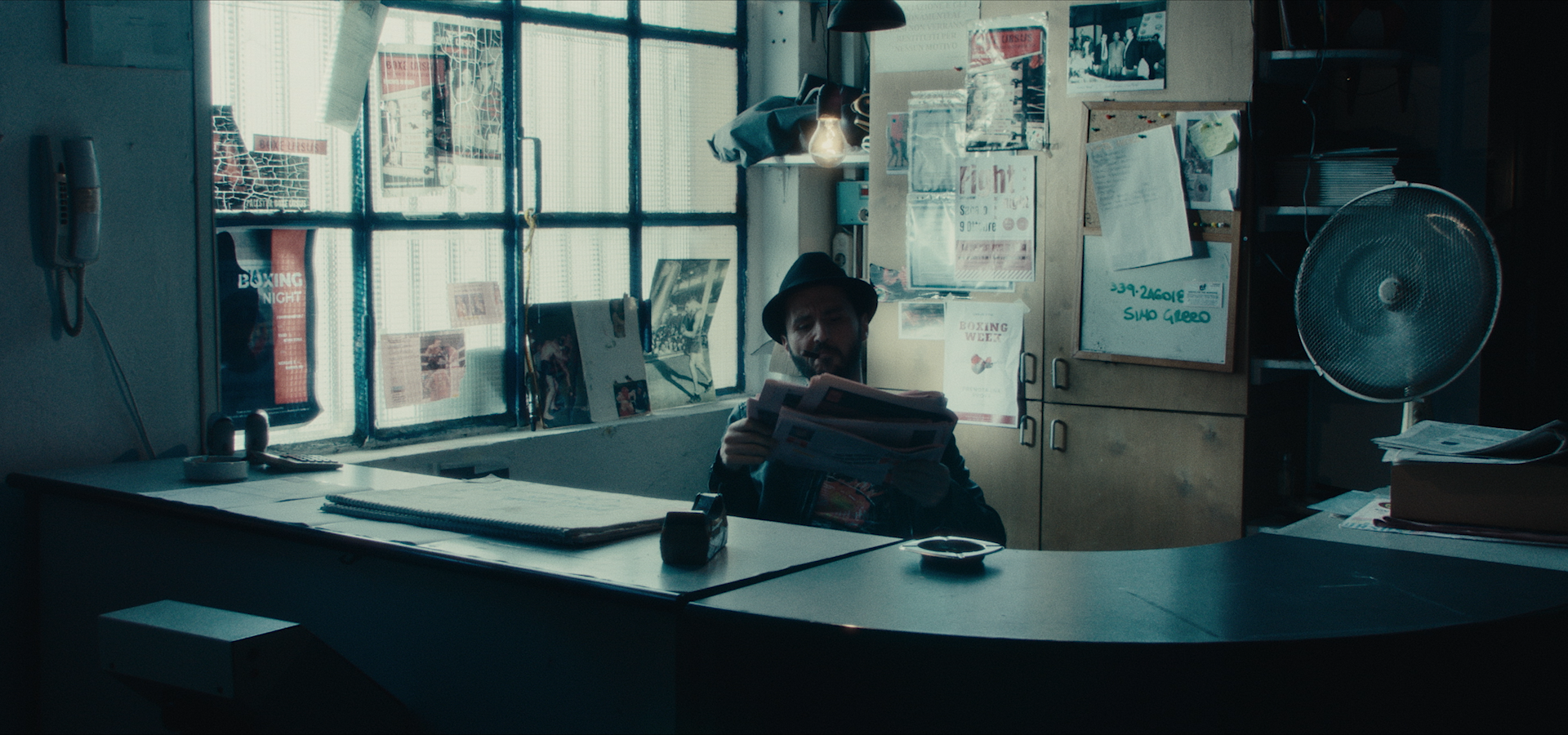 A man reading a newspaper behind a desk in a boxing gym