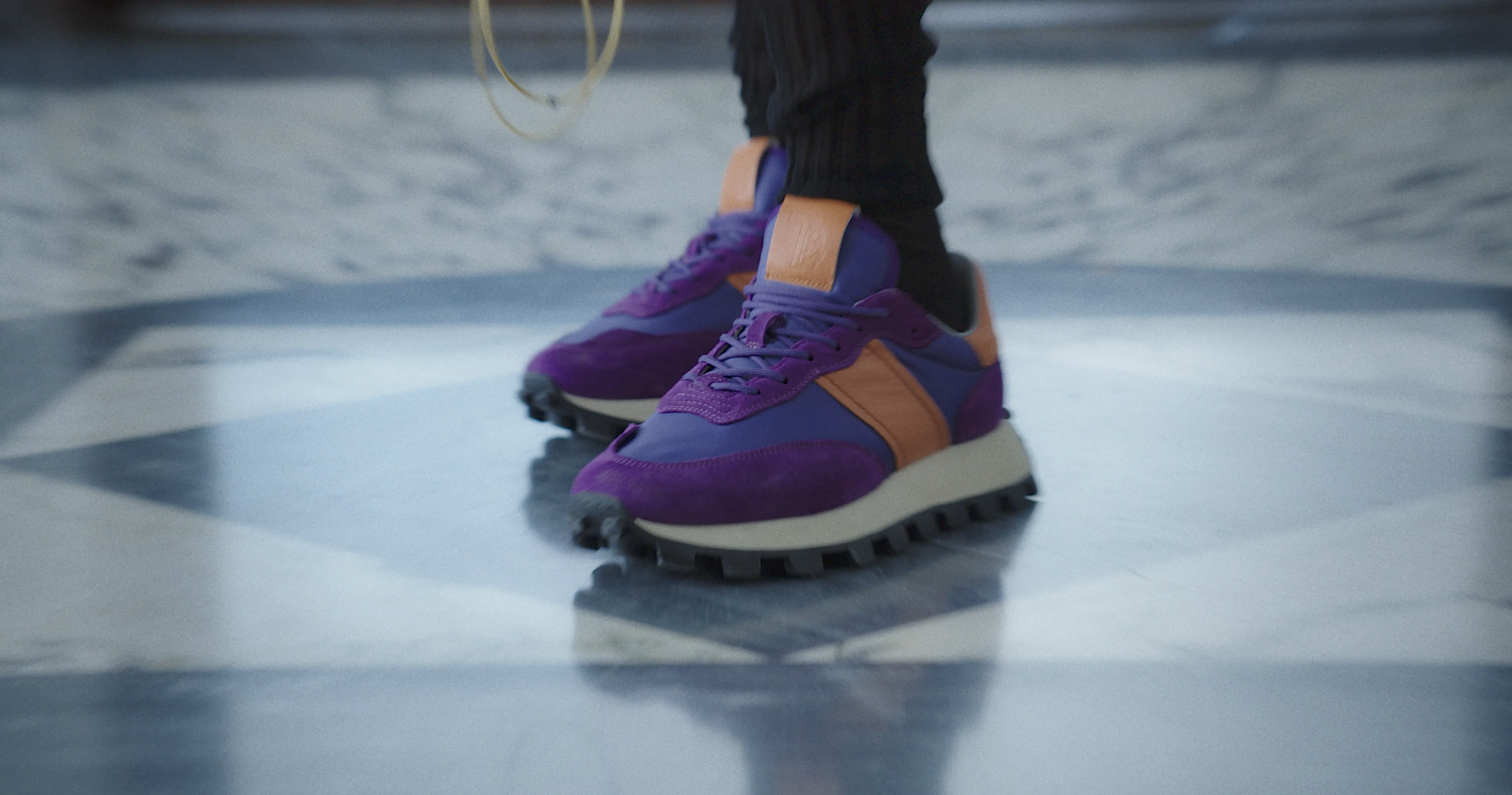 A close-up of purple and orange TOD’S sneakers on a marble floor